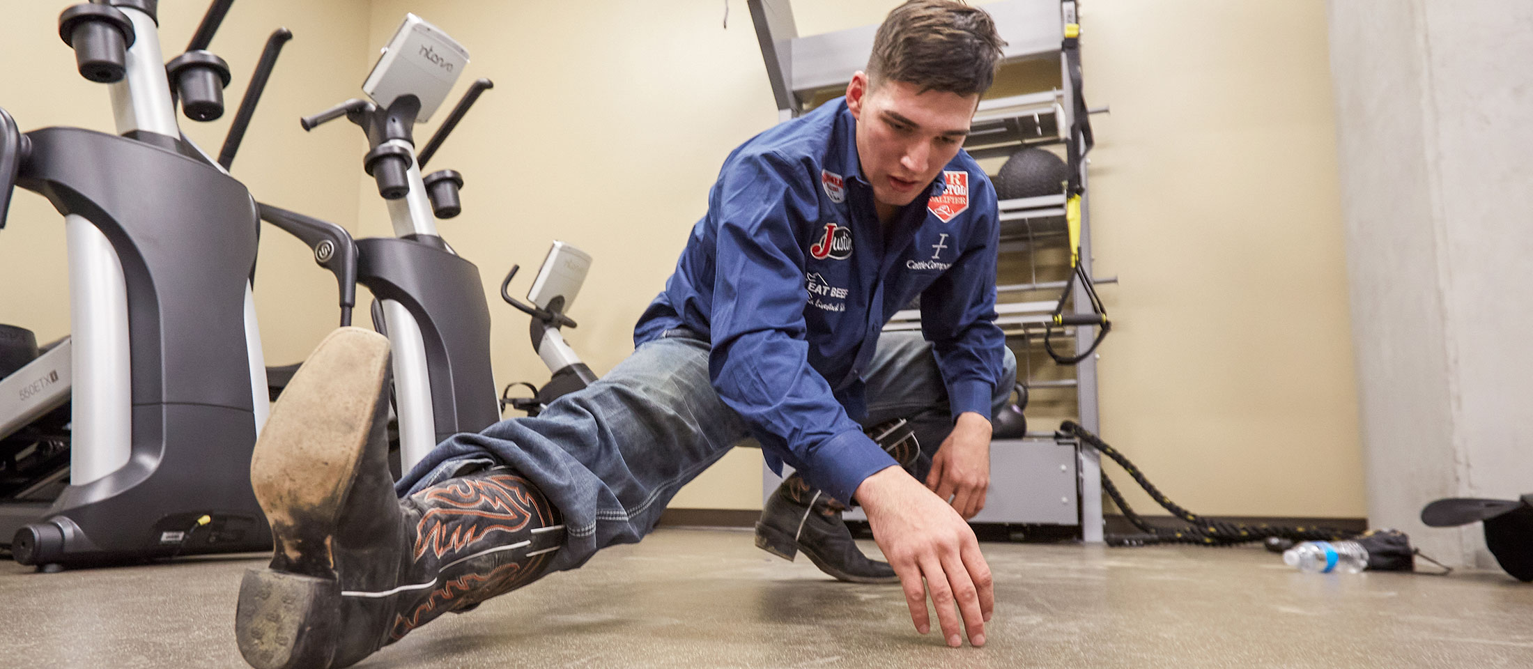 Jess Pope stretches before rodeo wearing western clothes and cowboy boots.